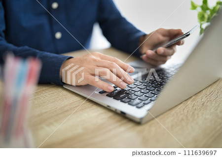 一名中年男子一邊看電腦一邊操作智慧型手機的手 111639697