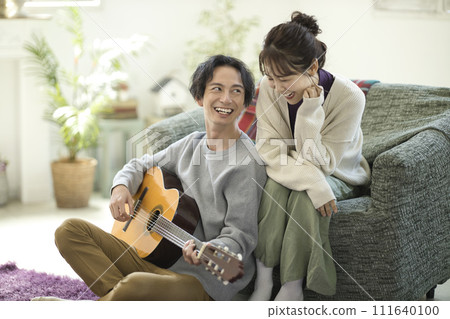Young couple sitting on sofa and singing while playing guitar 111640100