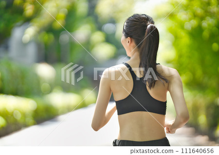 Rear view of a young woman in sportswear running in the greenery Rear view of a young woman in sportswear running in the greenery 111640656