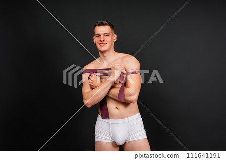 Young bodybuilder working out with rubber band over white and dark background Young bodybuilder working out with rubber band over white and dark background 111641191