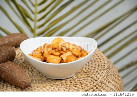 Organic manioca or cassava chips in bowl and tapioca tuber. Indonesia popular hot spicy snacks. Close up. Copy space. 111641239