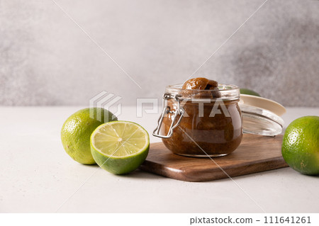 Traditional Sri Lankan Lime Pickle of lime, salt, chilli, pepper in glass preserve jar on gray background. Close up. Copy space. 111641261
