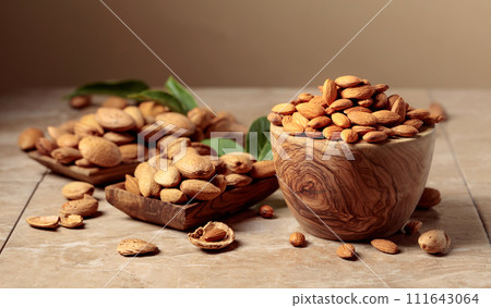 Almond nuts in wooden dishes on a ceramic table. 111643064