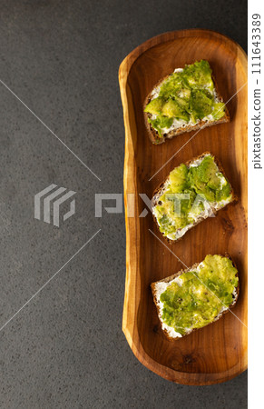 toast with cream cheese and avocado on a wooden plate, dark background 111643389