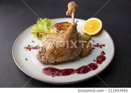Duck leg confit with Brussels sprouts, baked potatoes, thyme, orange and lingonberry sauce. Traditional French cuisine. Selective focus, close-up, black background. Duck leg confit with Brussels sprouts, baked potatoes, thyme, orange and lingonberry sauce. Traditional French cuisine. Selective focus, close-up, black background. 111643492