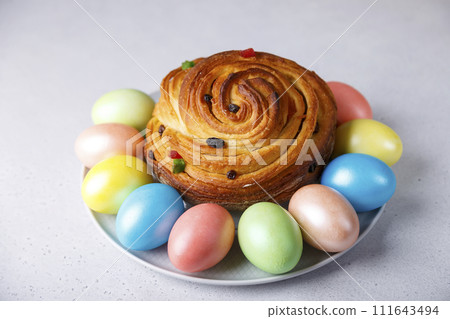 Craffin (Cruffin) with raisins and candied fruits. Traditional Easter Bread Kulich and painted eggs on a gray background. Easter Holiday. Close-up, selective focus. 111643494