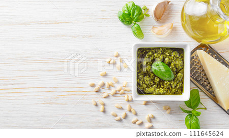 Homemade pesto sauce in small square jar and ingredients for pasta on white wooden background Homemade pesto sauce in small square jar and ingredients for pasta on white wooden background 111645624