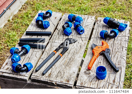 Compression fittings for connecting HDPE pipes lie on table next to hand tools. Compression fittings for connecting HDPE pipes lie on table next to hand tools. 111647484