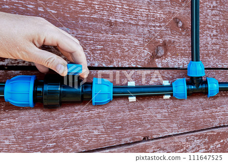 Closeup of hand shutting off water supply to an outdoor plastic water supply by turning lever on ball valve. Closeup of hand shutting off water supply to an outdoor plastic water supply by turning lever on ball valve. 111647525