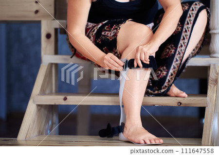 Woman puts on plastic ankle foot orthosis to support instable ankle and drop foot. Woman puts on plastic ankle foot orthosis to support instable ankle and drop foot. 111647558