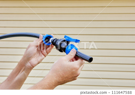 Adding ball valve as connecting fitting to an outdoor drinking water supply made of flexible plastic pipes, plumber uses screw compression clamp to make connection. Adding ball valve as connecting fitting to an outdoor drinking water supply made of flexible plastic pipes, plumber uses screw compression clamp to make connection. 111647588
