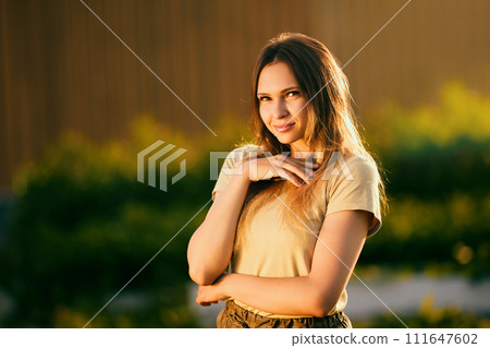 Portrait photography during golden hour, beautiful young Caucasian woman posing for photographer near rural house on summer evening, half length portrait of slender European female. 111647602