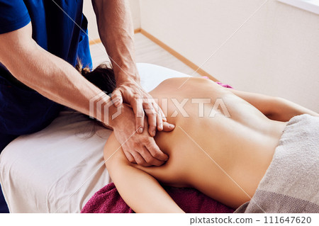 Massage therapist presses firmly with both hands on woman back in shoulder area when performing deep tissue massage. 111647620