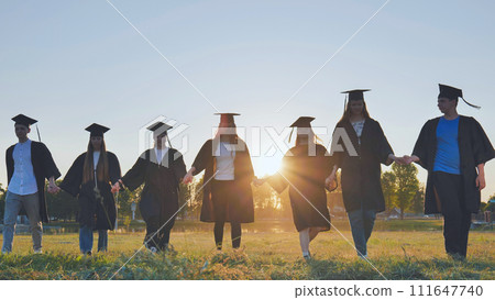 Graduate students walking through an evening meadow at sunset. Graduate students walking through an evening meadow at sunset. 111647740