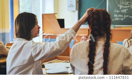 A friend strokes her friend's hair at her desk at school. 111647831