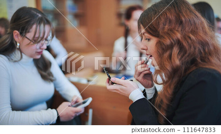 A schoolgirl paints her lips in class. 111647833