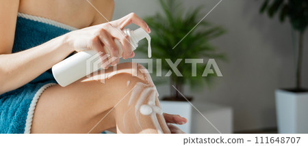 Anonymous woman pushing pump plastic soap bottle, using foam gel pump dispenser in bathroom. Close up view of female applying body lotion on leg during morning shower. Skin care, routine concept. Anonymous woman pushing pump plastic soap bottle, using foam gel pump dispenser in bathroom. Close up view of female applying body lotion on leg during morning shower. Skin care, routine concept. 111648707