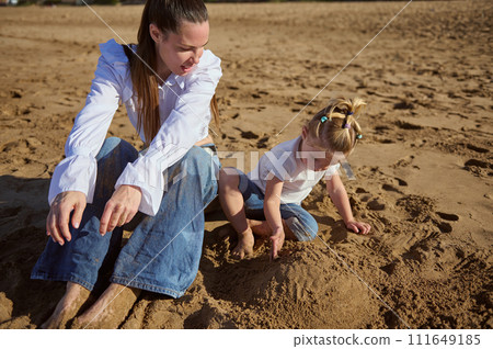 Happy family of a beautiful Caucasian single mother and daughter playing together on the beach, building sandy castle Happy family of a beautiful Caucasian single mother and daughter playing together on the beach, building sandy castle 111649185