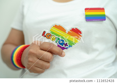 Asian lady wearing rainbow flag wristbands and hold heart, symbol of LGBT pride month celebrate annual in June social of gay, lesbian, bisexual, transgender, human rights. 111652428