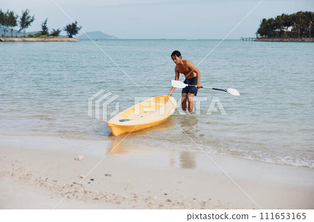 Happy asian man enjoying a summer vacation kayaking on a tropical beach with palm trees and clear blue ocean water. Happy asian man enjoying a summer vacation kayaking on a tropical beach with palm trees and clear blue ocean water. 111653165