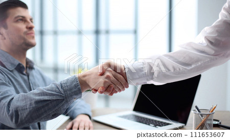 A male office worker shakes hands with a colleague in close-up 111653607