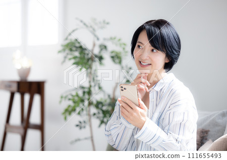 在客廳裡操作智能手機的中年女人 在客廳裡操作智能手機的中年女人 111655493