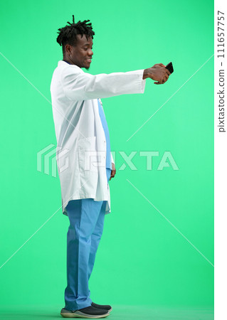 The doctor, in full height, on a green background, talking on the phone 111657757