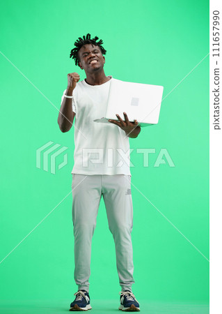 A man, full-length, on a green background, uses a laptop 111657990