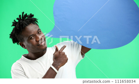 A man, close-up, on a green background, shows a blue comment sign A man, close-up, on a green background, shows a blue comment sign 111658034