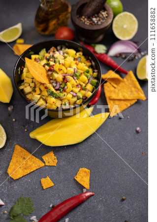Freshly made mango salsa in a black ceramic bowl, nacho chips and ingredients 111658882