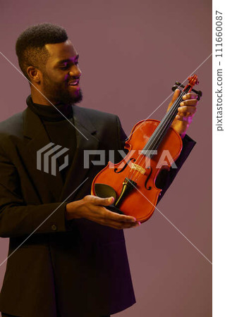 Elegant musician in suit playing violin against vibrant purple background for creative music concept 111660087