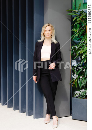 Beautiful young stylish businesswoman with in a black suit is standing near a gray wall in the city Beautiful young stylish businesswoman with in a black suit is standing near a gray wall in the city 111660881