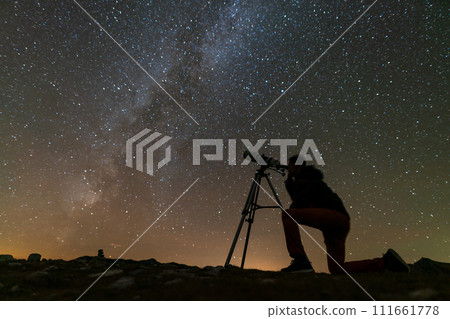 a man looks through a telescope on a tripod at the starry sky 111661778