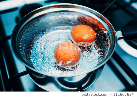 Stainless steel saucepan with boiling eggs for breakfast in boiling water on gas stove top view. Stainless steel saucepan with boiling eggs for breakfast in boiling water on gas stove top view. 111663654