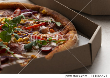 Large Pizza with sausages peppers and sweetcorn in open carton box on kitchen table extreme closeup Large Pizza with sausages peppers and sweetcorn in open carton box on kitchen table extreme closeup 111665471