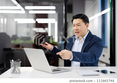 Angry angry boss at workplace inside office, senior mature asian man yelling at interlocutor, businessman using laptop for online meeting and remote video call. 111665748