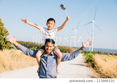 Dad carrying daughter with pinwheel smiling. Family joy near windmills represents global innovation in renewable energy. A moment of bonding joy and happiness in the community. Father Day 111666310