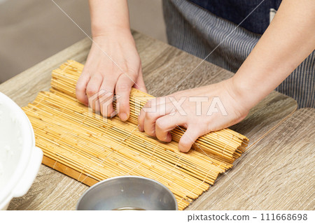 Hands of a woman making sushi with a makisu Hands of a woman making sushi with a makisu 111668698