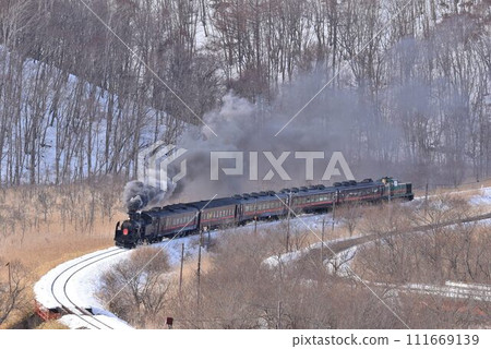 A steam locomotive traveling through the Kushiro Wetlands on a sunny winter day. Overhead view of the Temporary Pass railroad crossing. 111669139