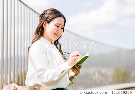 A young Asian business woman writing in a notebook, memo pad, and schedule book (interview, ideas, memos, plans) A young Asian business woman writing in a notebook, memo pad, and schedule book (interview, ideas, memos, plans) 111669299
