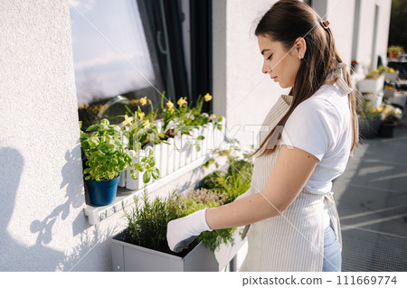 Attractive woman start landing on balcony. Young female in light striped overalls planting 111669774
