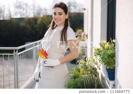 Young attractive female in overall with garden tools stand on balcony and preparing for landing 111669775