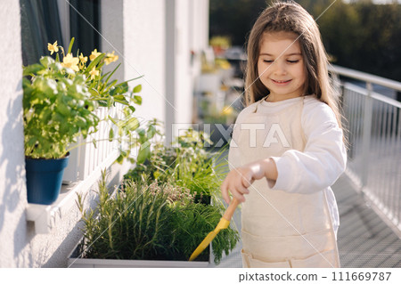 Cute little girl starting for landing on balcony. Side view of four year old girl use small shovel for soil Cute little girl starting for landing on balcony. Side view of four year old girl use small shovel for soil 111669787