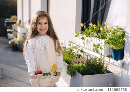 Cute girl plants greens in front of the window. Ripe harvest on balcony. Cute girl plants greens in front of the window. Ripe harvest on balcony. 111669788