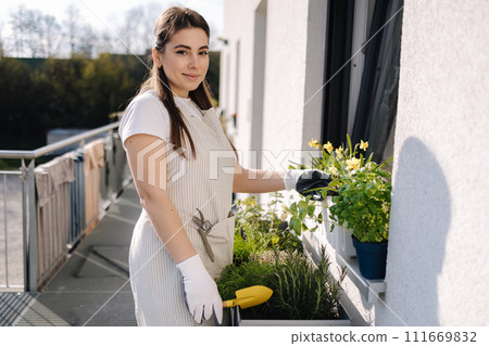 Attractive woman start landing on balcony. Young female in light striped overalls planting 111669832