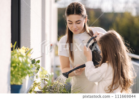 Mom watering plant with her adorable little daughter. Happy family gardening on balcony 111669844