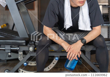 Young Asian man taking interval breaks at the gym (hydration/protein) Young Asian man taking interval breaks at the gym (hydration/protein) 111669962