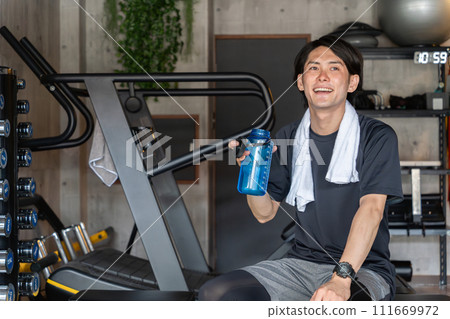 Young Asian man taking interval breaks at the gym (hydration/protein) 111669972