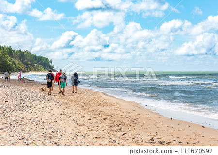 Back view of group of people walking along the seashore on a sunny day with dog. Back view of group of people walking along the seashore on a sunny day with dog. 111670592