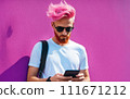 Hipster guy with pink hair uses a smartphone against a multicolored street wall. Summer concept. The style of Generation Z. 111671212